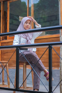 Portrait of young woman sitting by railing