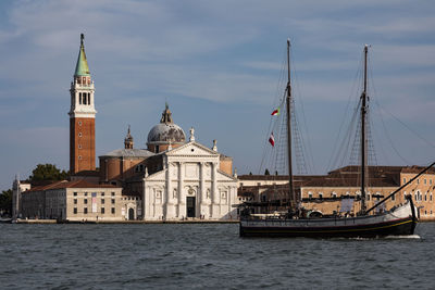 Sailboats in sea by buildings against sky