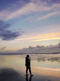 Full length of woman standing at beach against sky during sunset