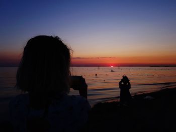 Silhouette people looking at sea against sky during sunset