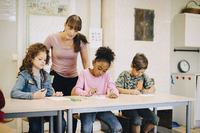 Teacher looking at students writing at desk in elementary classroom