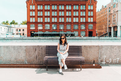 Full length of woman sitting on bench against building in city