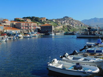 Boats moored at harbor against clear blue sky