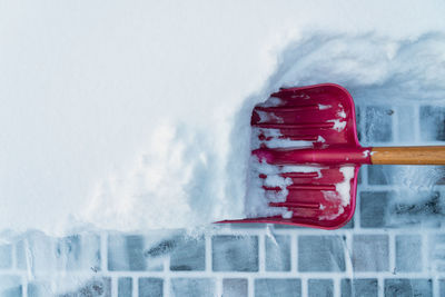 A red snow shovel with a wooden handle cleans a thick layer of snow from a paving slab. 