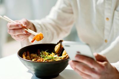 Midsection of person holding food and phone in restaurant