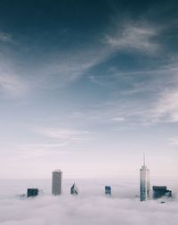 High section of skyscrapers amidst clouds against sky