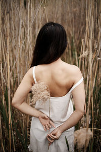 Back view of young woman standing against dry plants