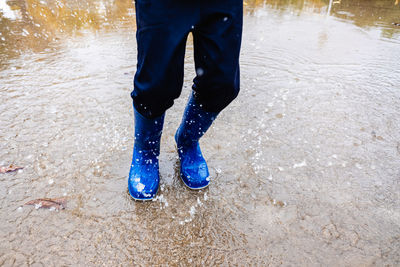 Low section of boy wearing boots jumping in puddle