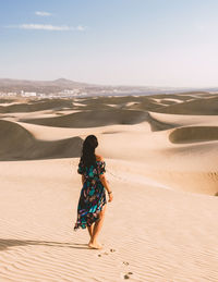 Rear view of woman walking at beach against sky