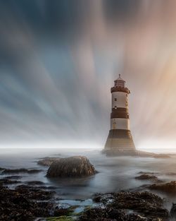 Lighthouse amidst sea and buildings against sky