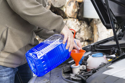 Midsection of man pouring blue liquid in car engine