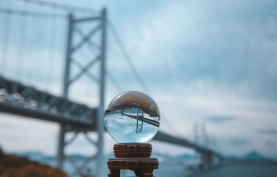 Close-up of crystal ball on bridge against sky