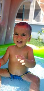 Portrait of smiling shirtless baby boy sitting in wading pool