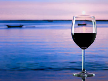 Close-up of wineglass against sea during sunset