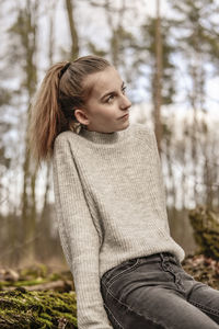 Teenage girl looking away while sitting in forest