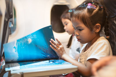 Side view of girl reading book while traveling in airplane