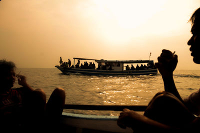 Cropped image of men smoking cigarette while sitting in boat on sea during sunset