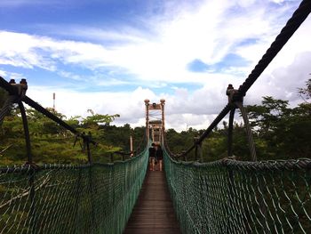 Footbridge over landscape against cloudy sky