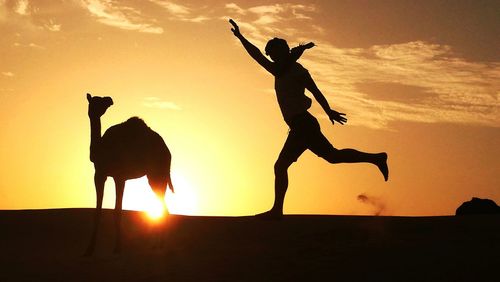Silhouette man jumping on landscape against sky during sunset