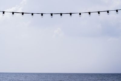 Low angle view of light bulbs hanging over sea against sky