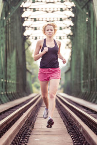 Full length portrait of woman running on railroad tracks