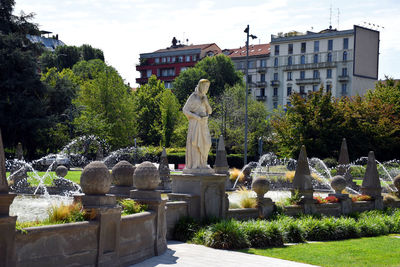 Statue by fountain in park against sky