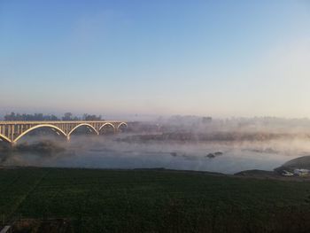 Arch bridge over field against sky during foggy weather