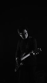 Man playing guitar against black background