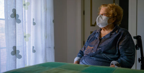 Portrait of man sitting on window at home