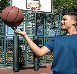 Smiling man playing with ball with basketball court