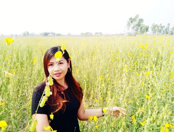 Portrait of smiling young woman with yellow flowers in field