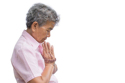 Side view of senior woman with hands clasped praying against white background