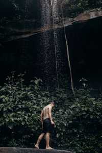 Full length of shirtless man standing at waterfall