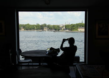 Silhouette woman photographing lake while sitting at table