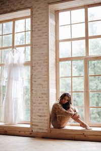 Woman sitting on window sill at home