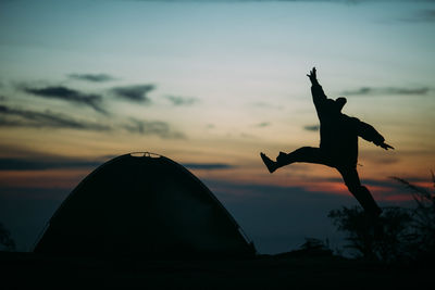 Silhouette man jumping by tent against sky