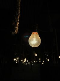 Low angle view of illuminated light bulb hanging at night