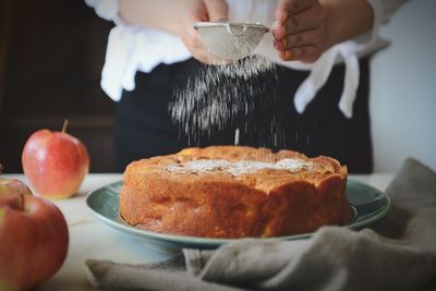 Midsection of person sprinkling powdered sugar on cake at kitchen