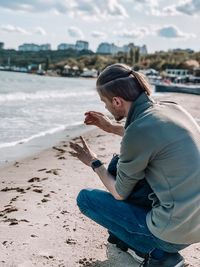 Man gesturing while crouching at beach