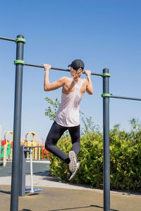  happy woman in sportclothes working out on the sports ground in sunny summer day, doing pull ups