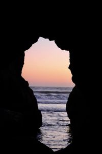 Silhouette rock formation on beach against sky during sunset