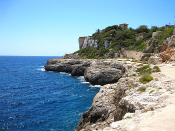 Rock formations by sea against clear blue sky