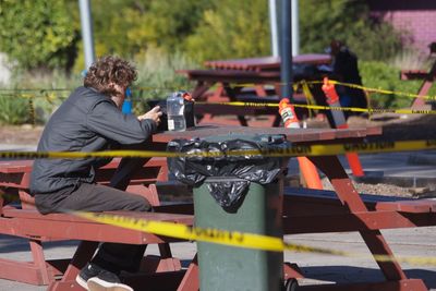 Side view of man sitting at picnic table amidst cordon tape