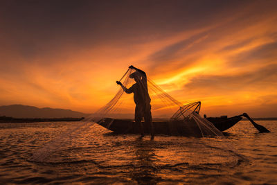 Fisherman fishing in lake against orange sky during sunset