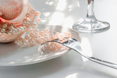 Close-up of pearls with seashell and fork in plate on table