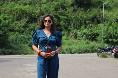 Portrait of young woman wearing sunglasses standing on road