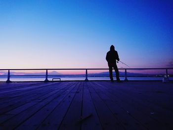 Rear view of silhouette fishing man standing against sea during sunset