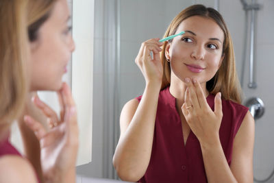 Brazilian woman shaving her eyebrows by razor at home. pretty woman using razor on bathroom.