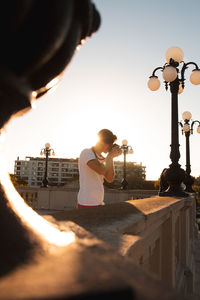 Woman standing by street light in city against sky during sunset