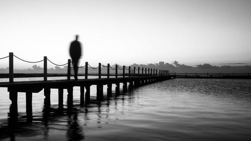 Silhouette man on jetty against sky during sunset